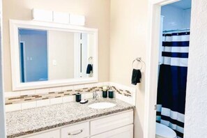 Un baño con un lavabo blanco, un espejo y una cortina de ducha a rayas.