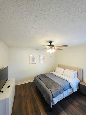 Un dormitorio con cama, ventilador de techo, televisor y obras de arte enmarcadas en la pared.