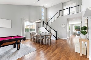 A spacious living area with a pool table, dining table, and chairs, a staircase with black railings, and a view of the outdoors. - Wine Country Retreat 5BR w/ Hot Tub (American Canyon)