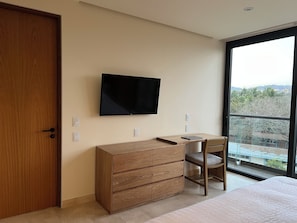 Een slaapkamer met een houten dressoir, een flatscreen televisie aan de muur, een bed en een groot raam met uitzicht op de natuur.
