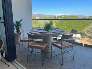 A round table with six chairs, a potted plant, and a view of a mountainous landscape. - BEAUTIFUL BEACHFRONT APARTMENT (Cruz de Huanacaxtle)