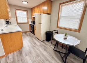 Una cocina compacta con armarios de madera, un refrigerador, un lavamanos y una mesa de comedor con sillas.