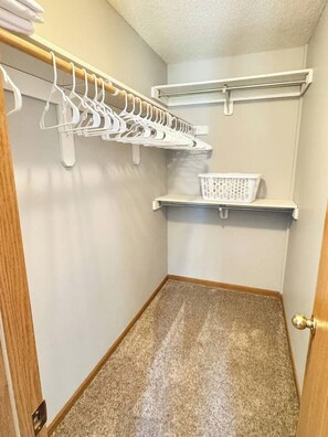 A small closet with a wooden door, a white hanging rack, and a white basket on a shelf.