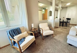 A living room with a sofa, two armchairs, a small table, a hanging plant, and a dining area with a table and chairs. - 511 Serenity on Shugart (Beatrice)