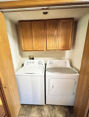 A compact laundry area with two washing machines and wooden cabinets above.
