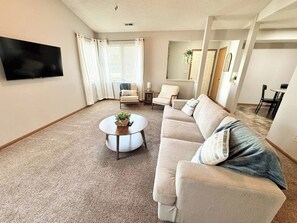 Una sala de estar con sofá, sillones, una mesa de centro y un televisor de pantalla plana.