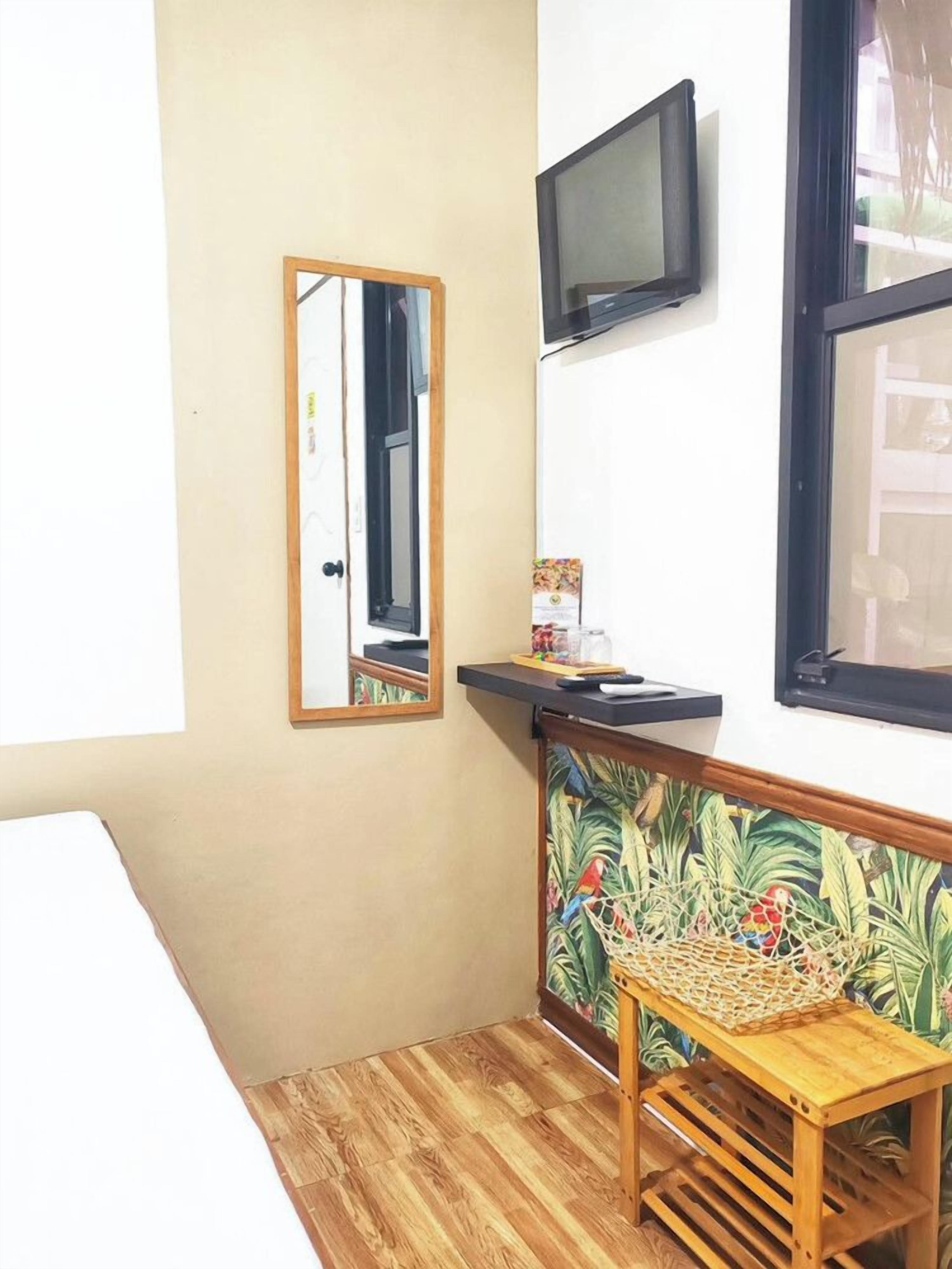 A small room with a wooden floor, a mirror, a television mounted on the wall, and a small table with a woven basket.