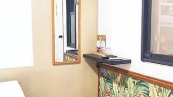 A small room with a wooden floor, a mirror, a television mounted on the wall, and a small table with a woven basket.