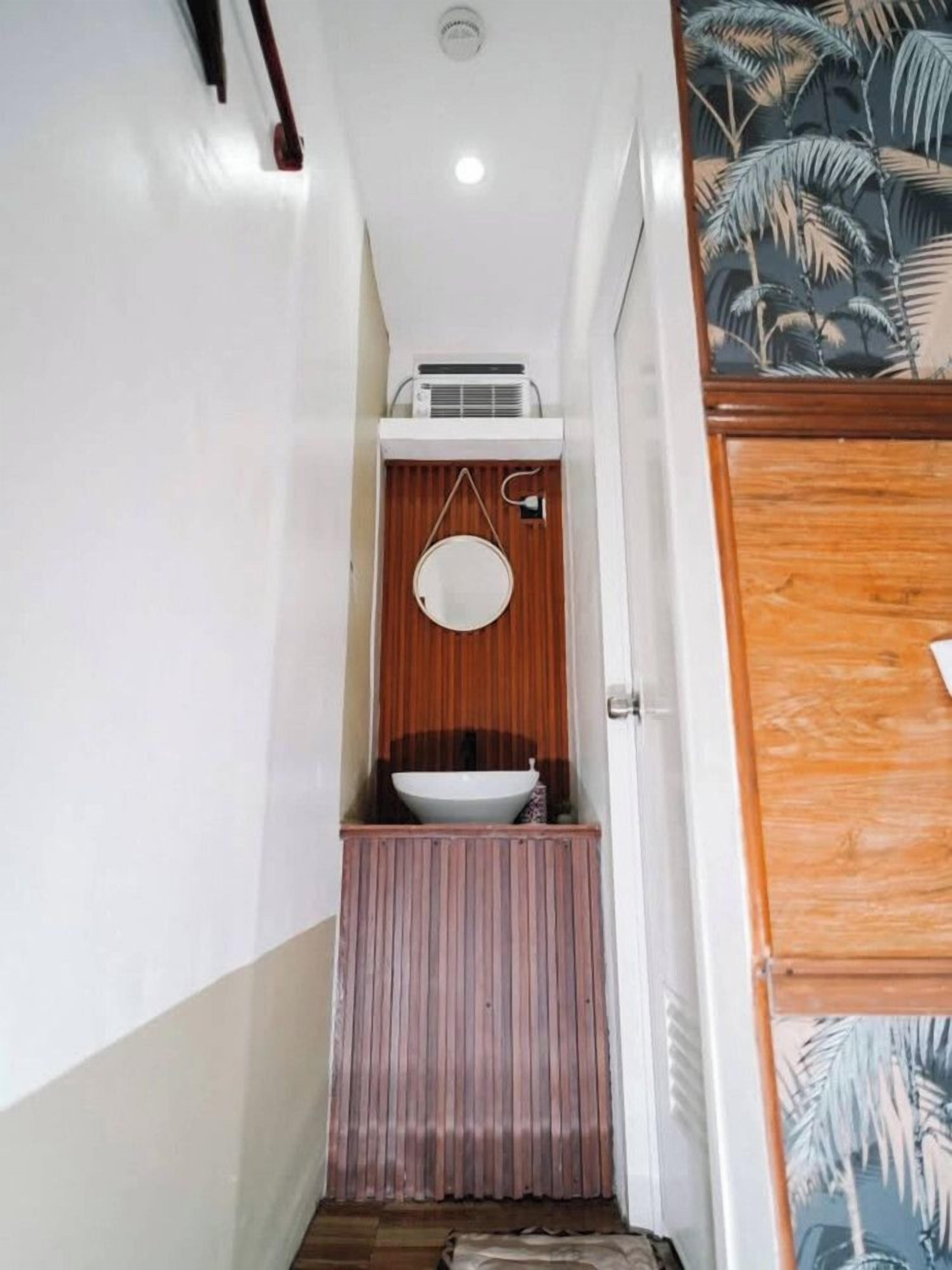 A narrow hallway with a wooden door on the right, a white wall, and a small window with a wooden frame.
