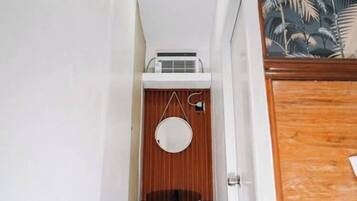 A narrow hallway with a wooden door on the right, a white wall, and a small window with a wooden frame.