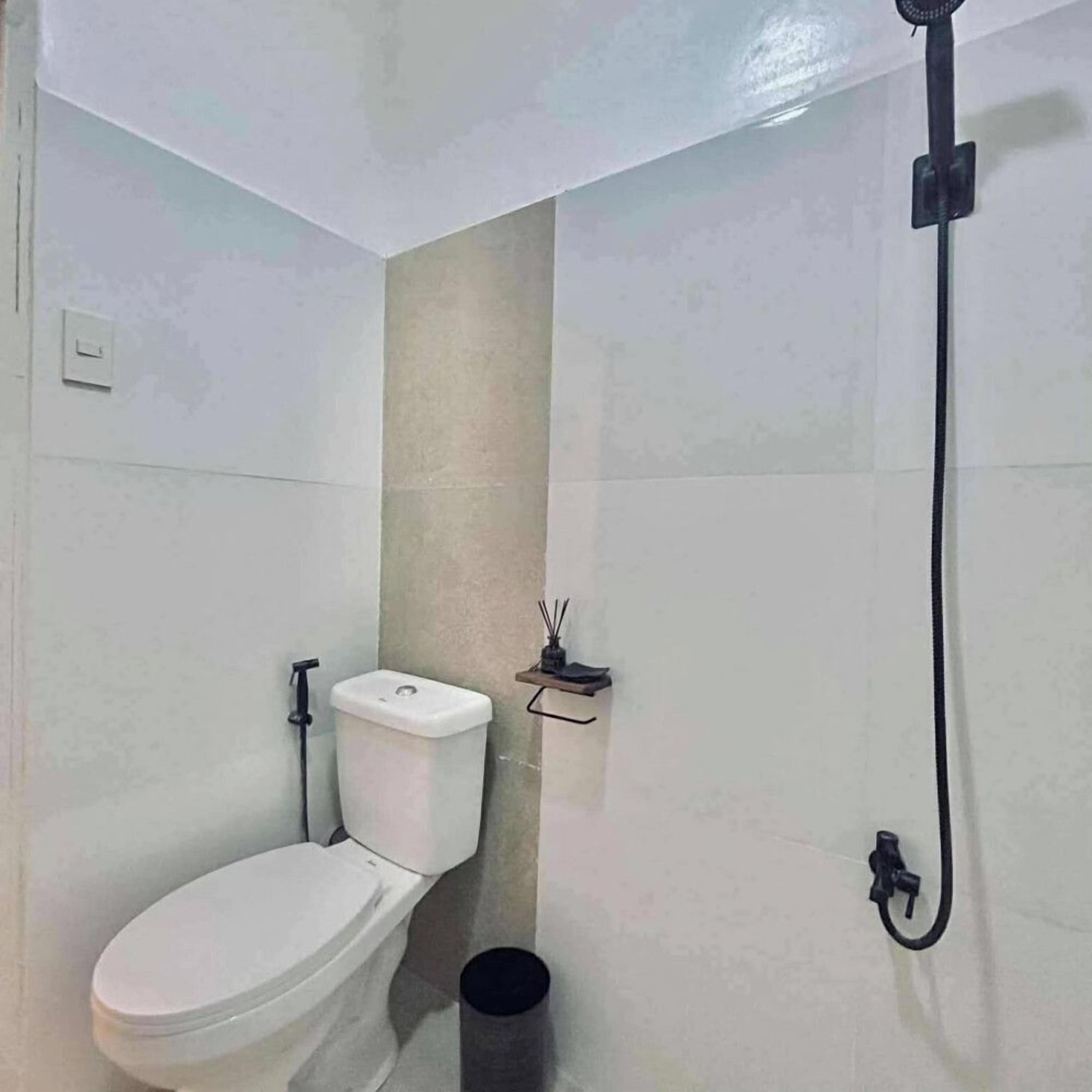 A small bathroom with a toilet, a shower, and a waste bin.