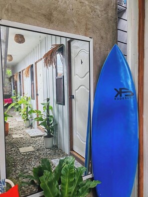 Een gang met deuren naar kamers, een blauw surfplank en potplanten.