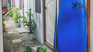 A corridor with doors leading to rooms, a blue surfboard, and potted plants.