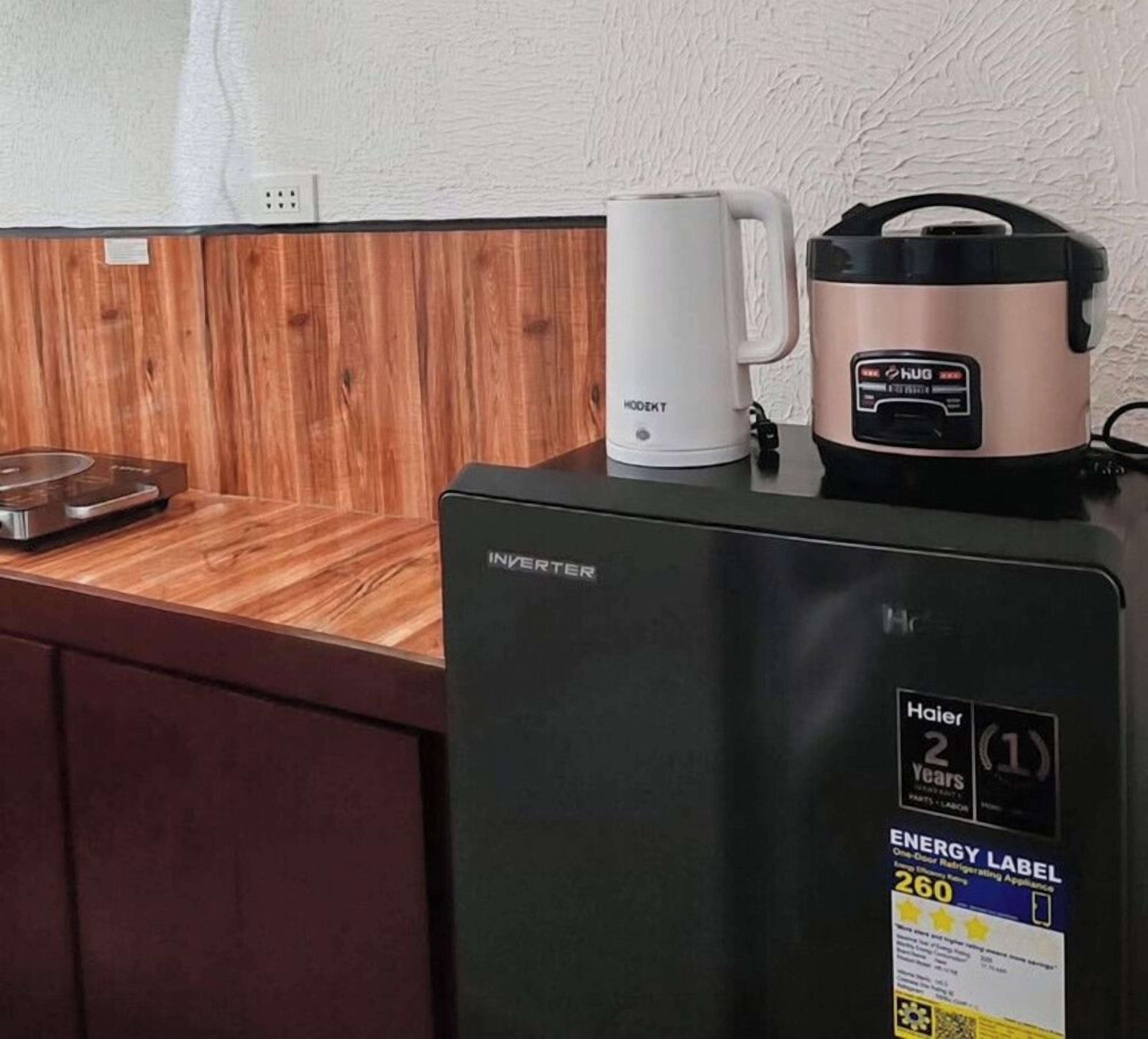 Une cuisine compacte avec un réfrigérateur noir, une machine à café blanche et un cuiseur à riz posé sur le plan de travail.