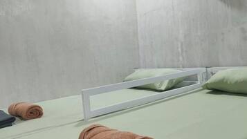 Een eenpersoonsbed met een wit frame, een groene matras en een opgerolde bruine handdoek.