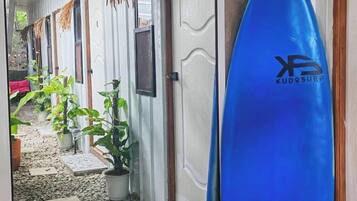 A hallway with a surfboard leaning against a door, potted plants, and a tiled floor.