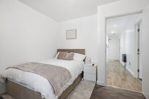Quarto com cama, mesa de cabeceira e televisão.
