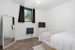 Ein Schlafzimmer mit einem Bett, einem Fernseher, einem Spiegel und einem Fenster mit Vorhängen.