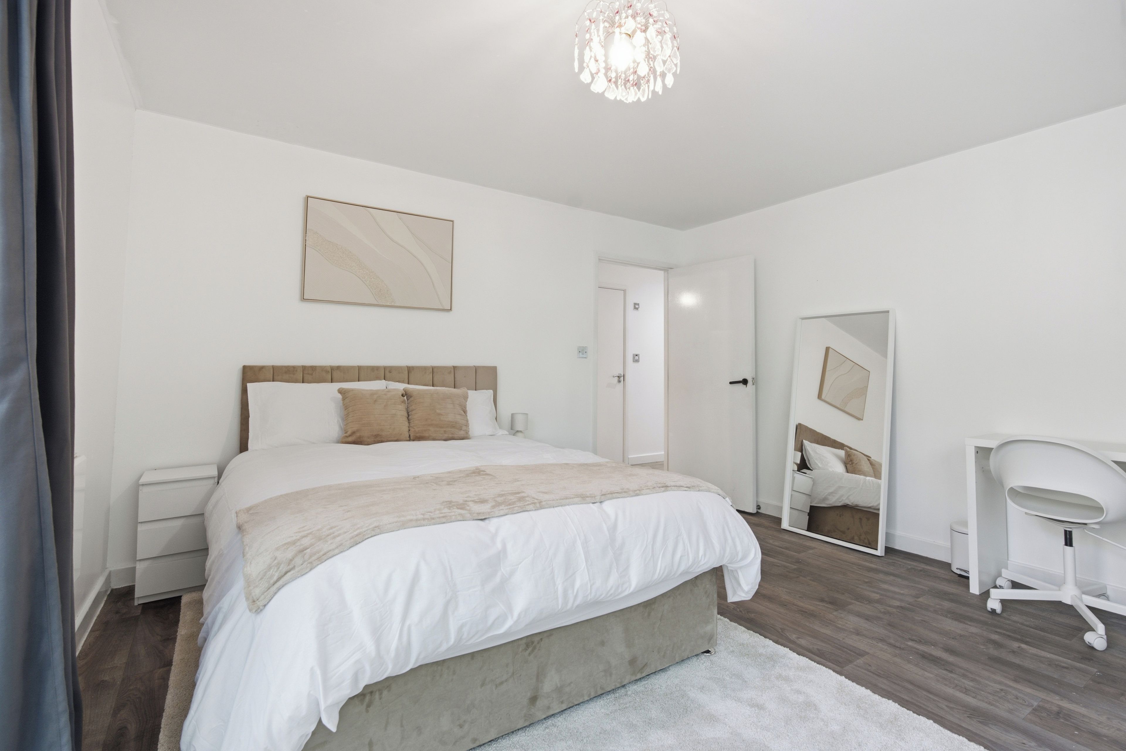 A modern bedroom with a large bed, a bedside table, a chair, a mirror, and a ceiling light fixture.