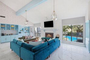 A spacious living room with a large blue sofa, a fireplace, and a view of a pool.