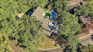 Vista aérea de una zona residencial con una casa de techo inclinado, un garaje visible y un patio con piscina azul.