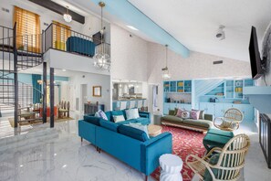 A spacious living area with a blue sofa, a dining table, and a kitchen in the background.