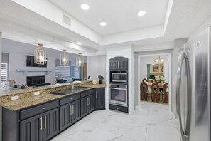 A modern kitchen with dark cabinetry, granite countertops, stainless steel appliances, and pendant lighting.