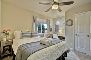 Ein Schlafzimmer mit Bett, Nachttischen, Schreibtisch, Stuhl, Deckenventilator und einer Tür.