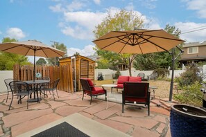 Eine Terrasse mit Gartenmöbeln, darunter ein Tisch und Stühle, sowie zwei große Sonnenschirme, die Schatten spenden.