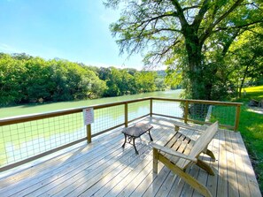 Eine Holzterrasse mit Bank und Tisch, mit Blick auf einen Fluss, umgeben von Bäumen.