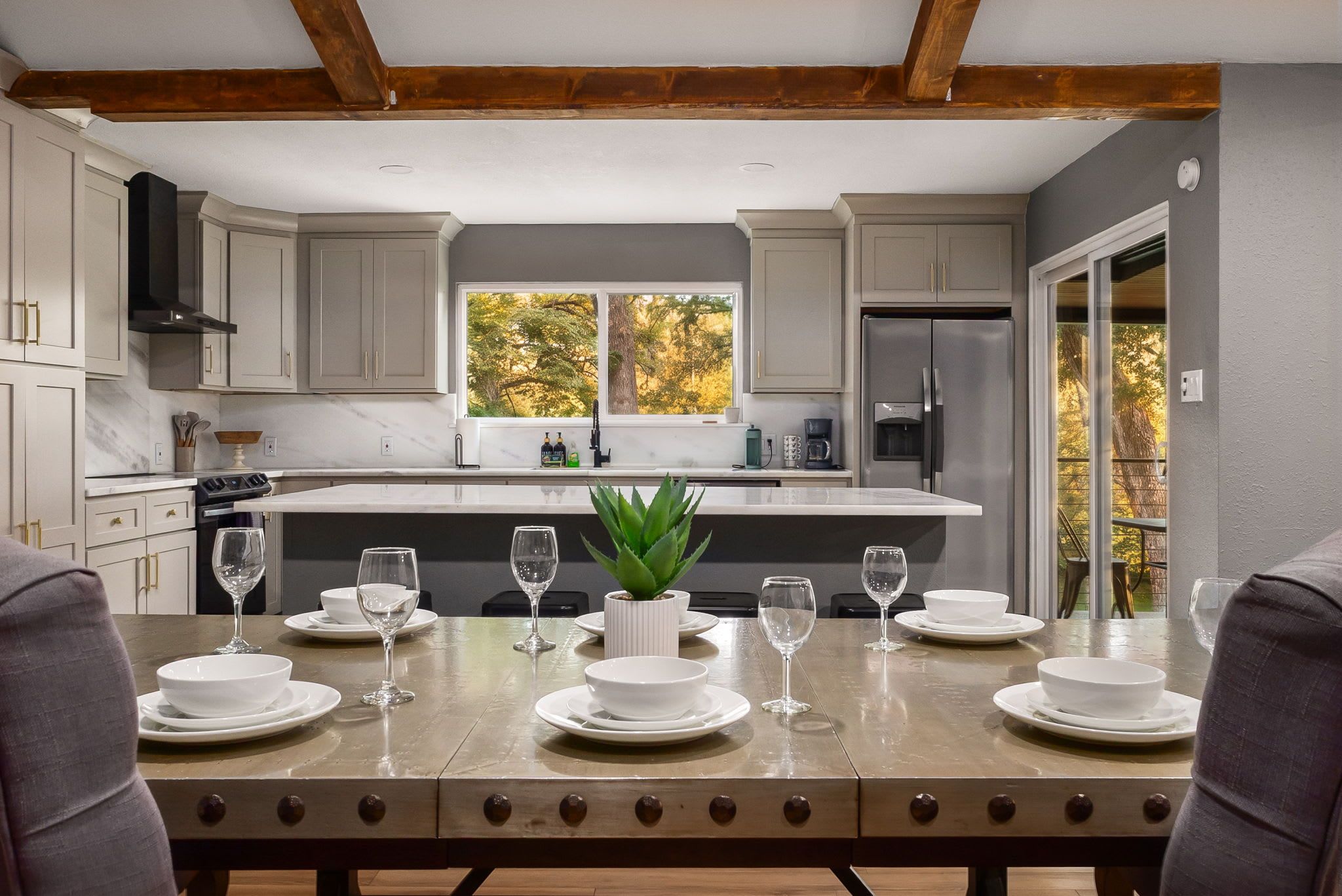 A modern kitchen with a central island, built-in appliances, and a view of trees through the window.