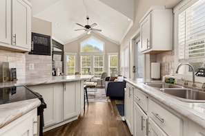 A modern kitchen with a central island, a dining area with a sofa, and a large window providing natural light. - Pets Welcome! Tiny House + Guadalupe River Access (New Braunfels)