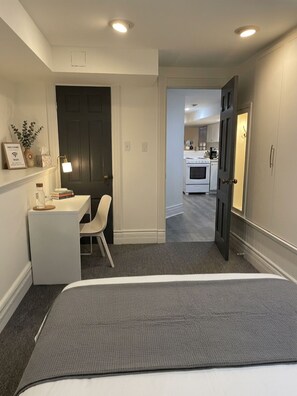 A hotel room with a bed, a desk, and a chair. There is a door leading to the kitchen. - Charming & Furnished Roncesvalles Suite. Pet Friendly! (Toronto)