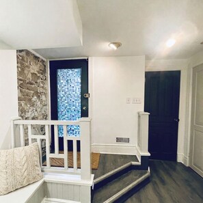 A staircase with a white railing, a stone accent wall, and a door with a blue mosaic panel. - Charming & Furnished Roncesvalles Suite. Pet Friendly! (Toronto)