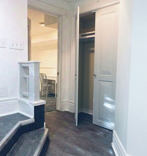 A hallway with a staircase leading to a room, a door to a closet, and a chair in the background. - Charming & Furnished Roncesvalles Suite. Pet Friendly! (Toronto)