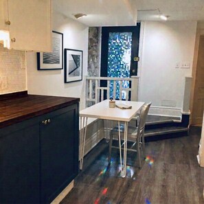 A dining area with a table and chairs, a wooden cabinet, and a window with a view. - Charming & Furnished Roncesvalles Suite. Pet Friendly! (Toronto)