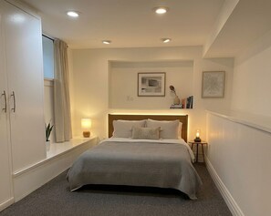 A bedroom with a bed, bedside tables, a window with curtains, and wall-mounted artwork. - Charming & Furnished Roncesvalles Suite. Pet Friendly! (Toronto)