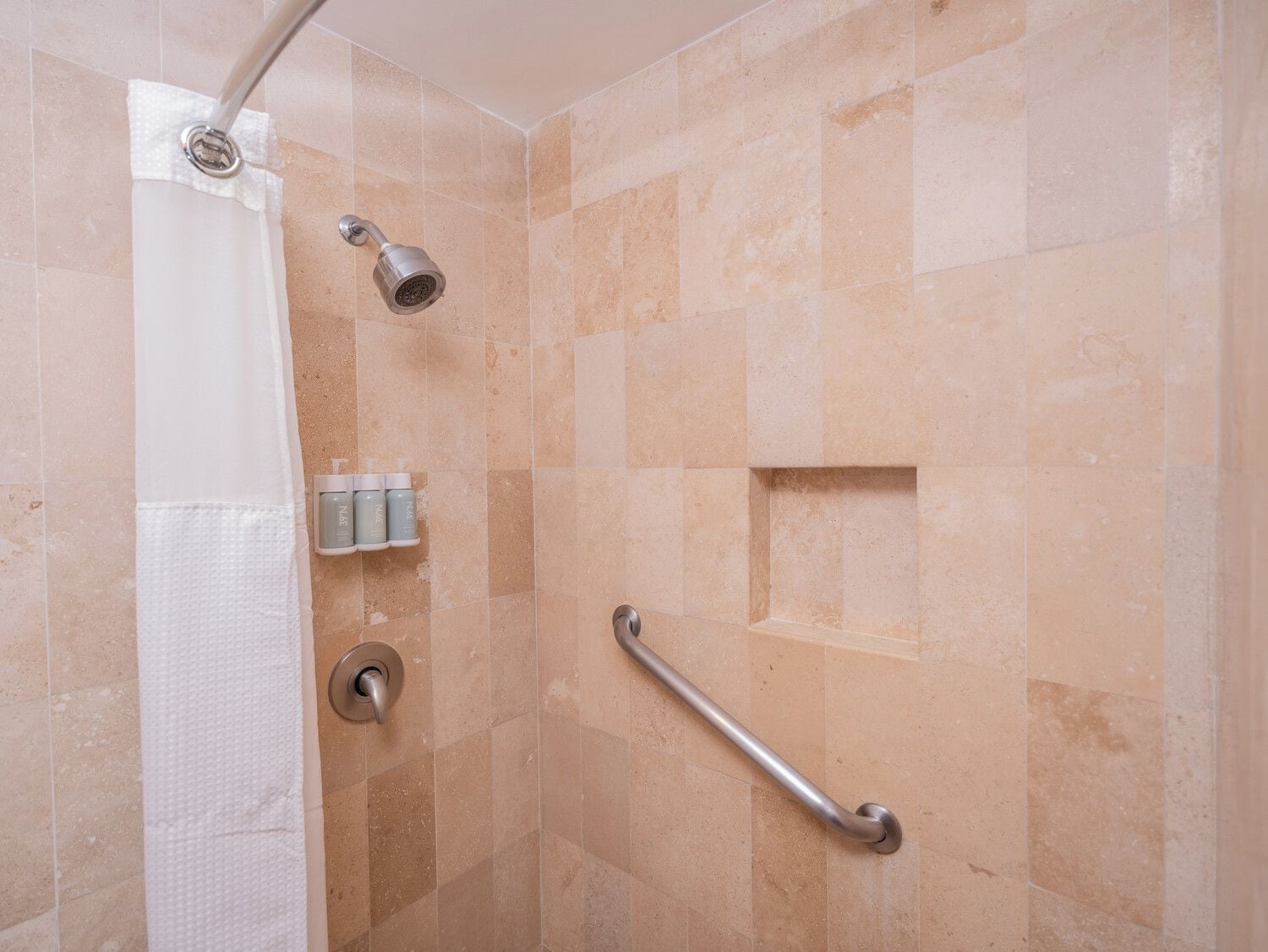A shower area with a handheld showerhead, a grab bar, and a towel dispenser.