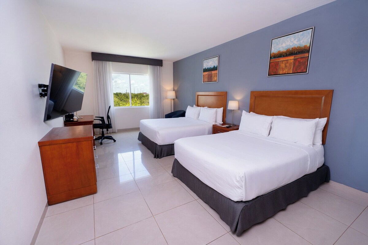 Habitación de hotel con dos camas, un escritorio, un televisor y una ventana con cortinas.