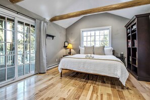 A bedroom with a large bed, a window, a bookshelf, and a view of the outdoors. - Oakwood Lodge! Secluded Forest Retreat w/ Hot Tub (Green Mountain Falls)