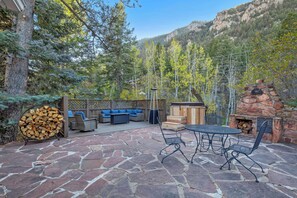 A patio with stone flooring, outdoor furniture, a fire pit, and a wooden deck. - Oakwood Lodge! Secluded Forest Retreat w/ Hot Tub (Green Mountain Falls)