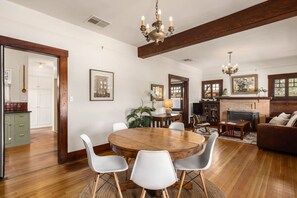 A dining area with a wooden table and chairs, a fireplace, and a living room with a sofa and a TV. - Charming historic bungalow in prime location (Tucson)