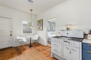 A compact kitchen with a gas stove, white cabinets, and a dining area with two chairs. - Charming historic bungalow near University (Tucson)