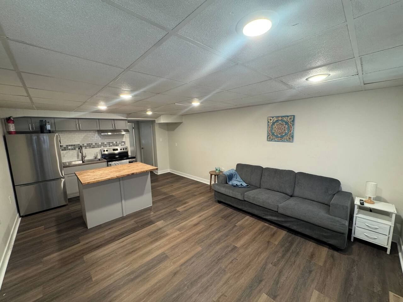 A modern kitchen with stainless steel appliances and a grey sofa in a living area with hardwood flooring.