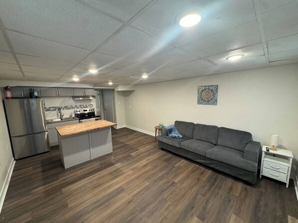 A modern kitchen with stainless steel appliances and a grey sofa in a living area with hardwood flooring.