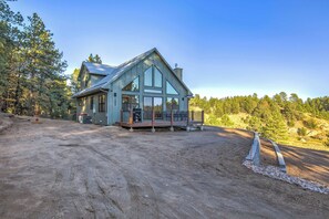 Une maison moderne à deux étages, dotée d’une grande terrasse et entourée d’un paysage boisé.