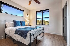 A bedroom with a bed, two nightstands, a ceiling fan, and two windows with views of trees. - Conestoga Creek! NEW Secluded Cabin w/Deck & Views (Florissant)