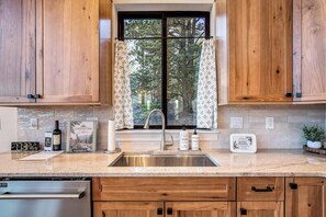 A kitchen with wooden cabinets, a stainless steel sink, and a window with curtains. - Conestoga Creek! NEW Secluded Cabin w/Deck & Views (Florissant)