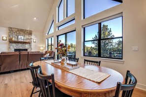 A spacious dining area with a large wooden table, surrounded by chairs, and a stone fireplace. - Conestoga Creek! NEW Secluded Cabin w/Deck & Views (Florissant)