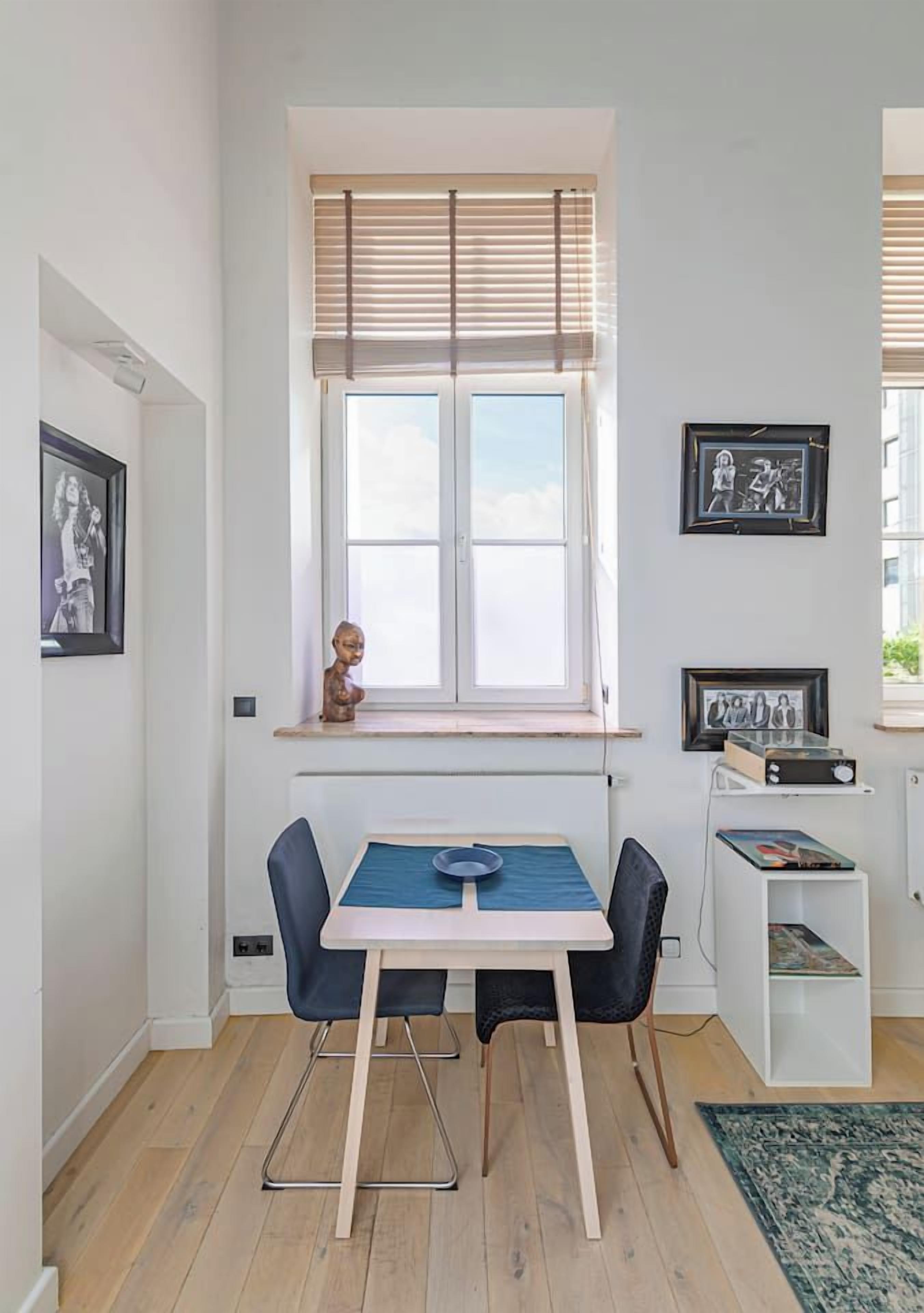 A room with a window, a table with chairs, and framed pictures on the wall.